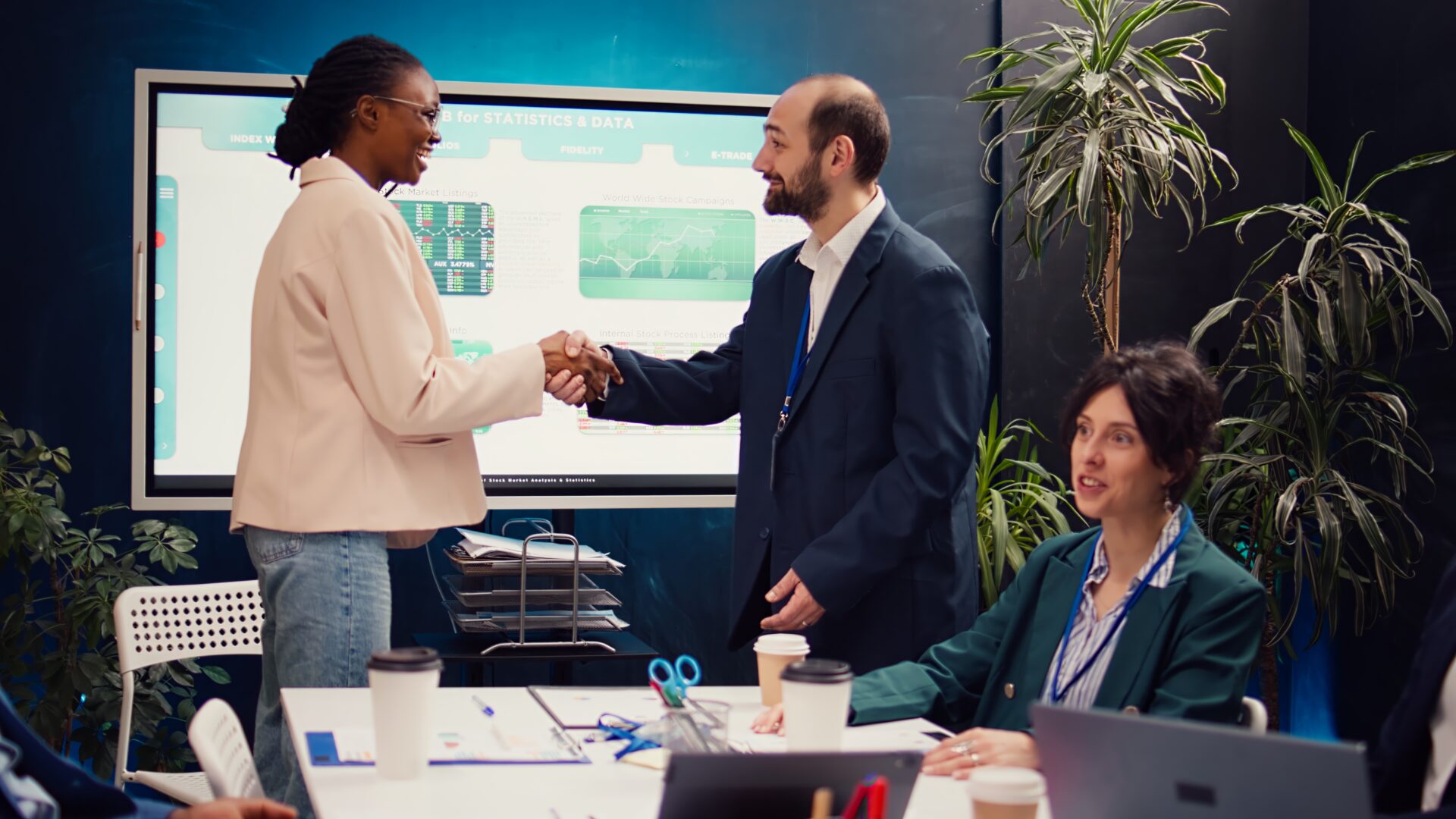 Business manager does handshake with a new employee during a briefing meeting, welcoming her to the team and presenting her to other staff members. Young man shaking hands with trainee. Camera B.